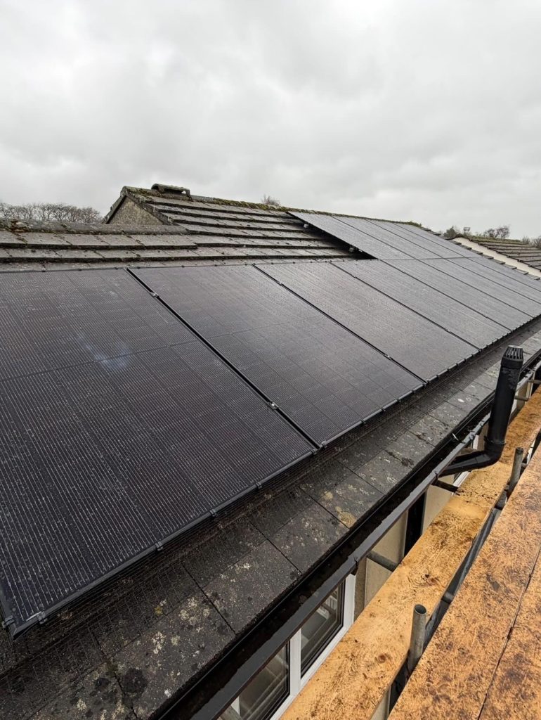 Yorkshire Dales Solar Installation | R&B Mechanical & Electrical Sloped roof covered with dark solar panels under a cloudy sky; scaffolding along the edge.